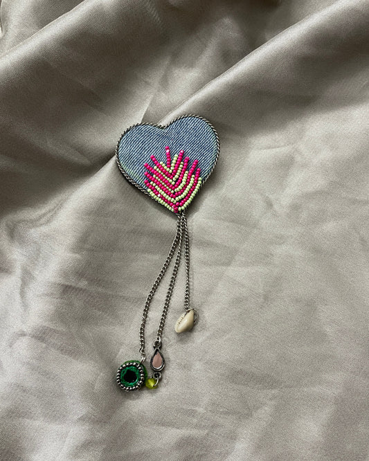 Heart-shaped embroidered pendant with beads on a textured fabric background